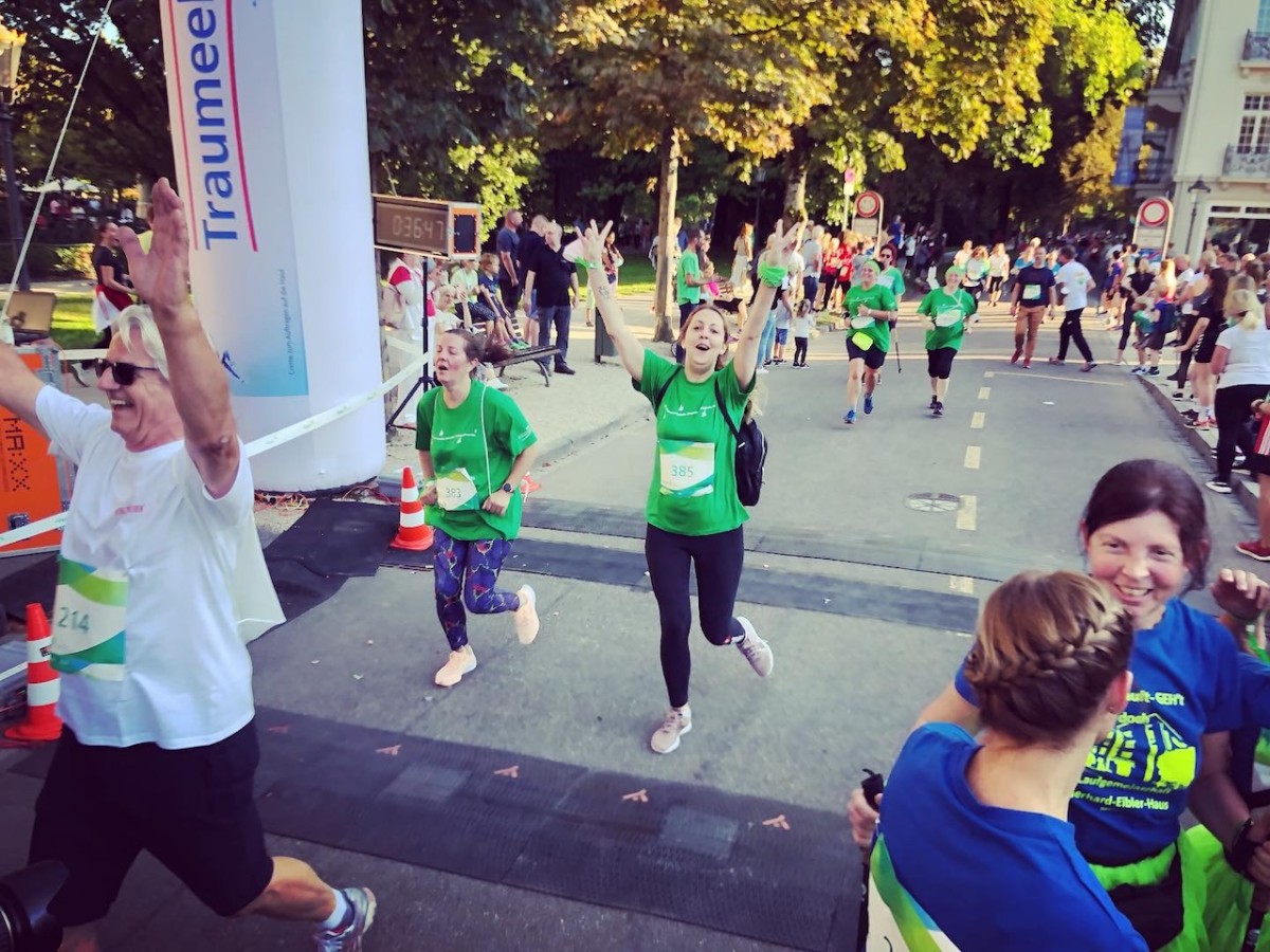 Läufer in grünen T-Shirts nehmen an einem Lauf teil, jubeln und laufen unter Straßenbäumen und Startschildern.