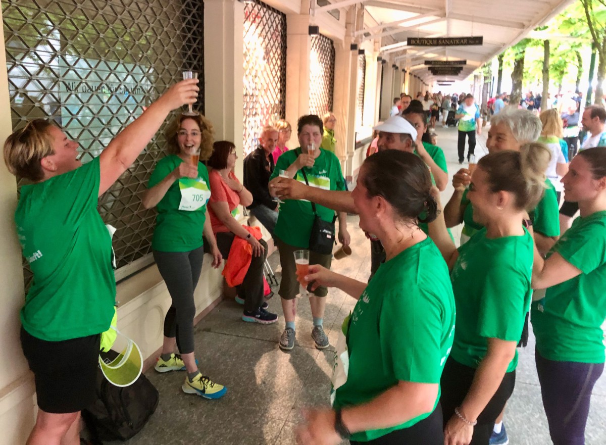 Gruppe von Menschen in grünen T-Shirts, die miteinander interagieren und Getränke halten.